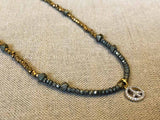 closeup of pave peace sign pendant hung on metallic bead choker