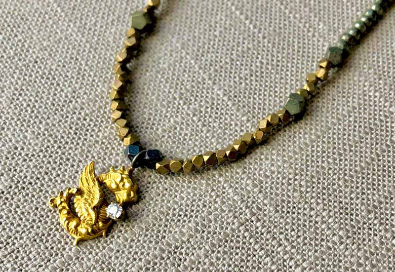 closeup of antique dragon pendant hung on metallic bead choker