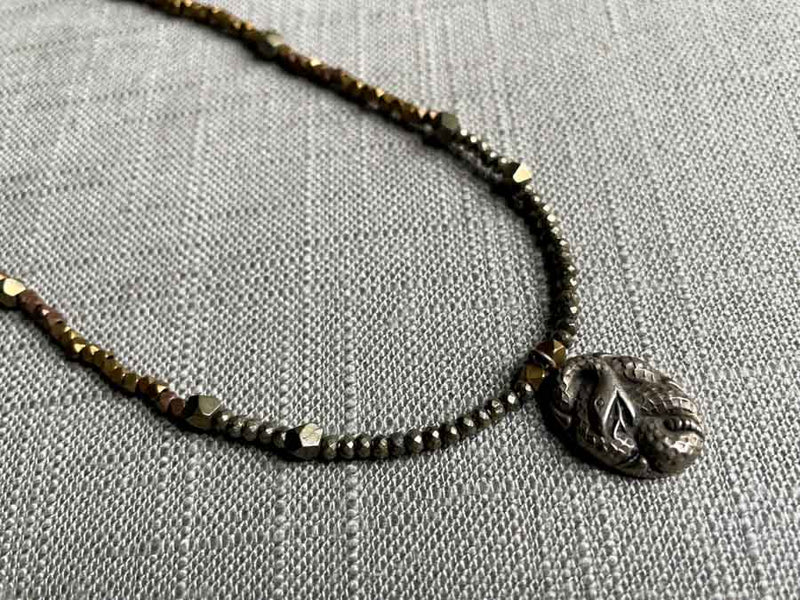 closeup of antique snake pendant hung on metallic bead choker