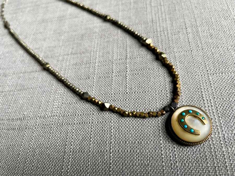 top view of antique horseshoe pendant with turquoise hung on metallic bead choker