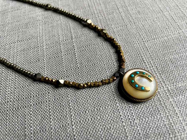 closeup of antique horseshoe pendant with turquoise hung on metallic bead choker