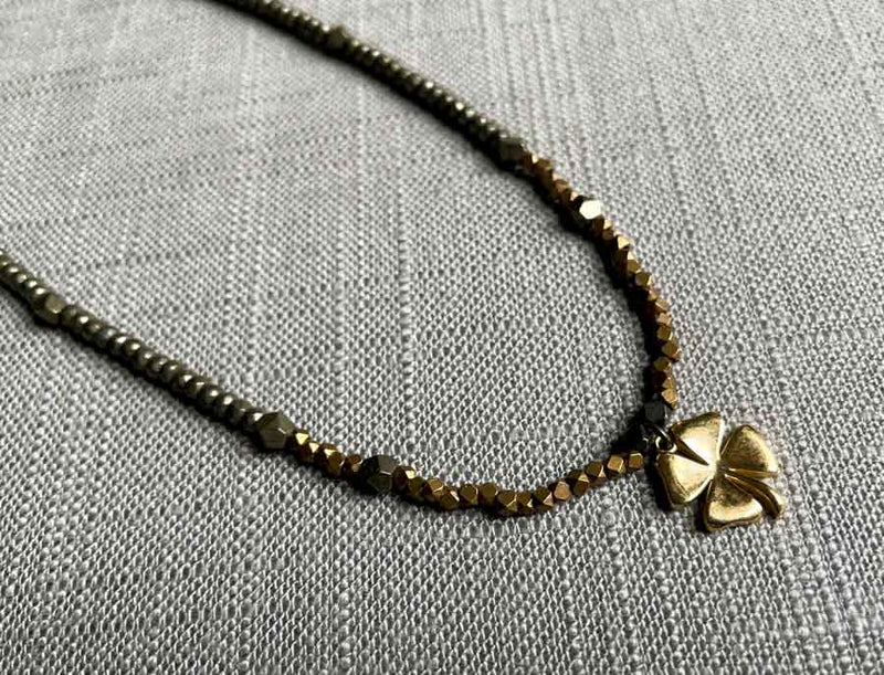 closeup of antique four leaf clover pendant hung on metallic bead choker