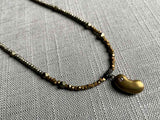 closeup of antique lucky bean pendant with diamond hung on metallic bead choker