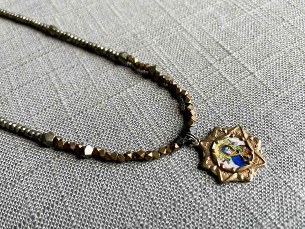 closeup of antique madonna and child pendant hung on metallic bead choker