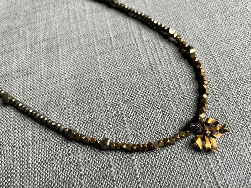 closeup of antique bow pendant hung on metallic bead choker