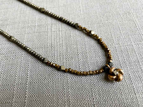 closeup of antique love knot pendant with diamond hung on metallic bead choker