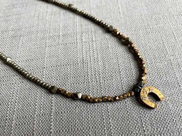 closeup of antique horseshoe pendant hung on a metallic bead choker