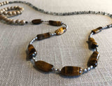 closeup of gemstone bead necklace comprising black and white tourmalated quartz, brown tigers eye, exotic wood and silver hematite