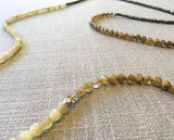 closeup of gemstone bead necklace comprising yellow jade, dark grey pyrite and beige rutilated quartz