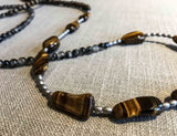 closeup of gemstone bead necklace comprising black and white tourmalated quartz, brown tigers eye, exotic wood and matte silver