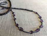 closeup of gemstone bead necklace comprising purple amethyst, tourmalated quartz, exotic wood and silver hematite