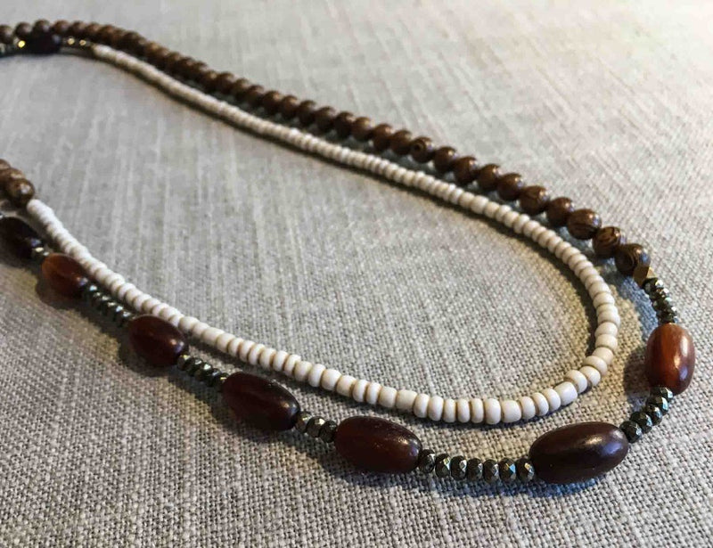 top view of gemstone bead necklace comprising white conch shell, brown horn, exotic wood and dark grey pyrite