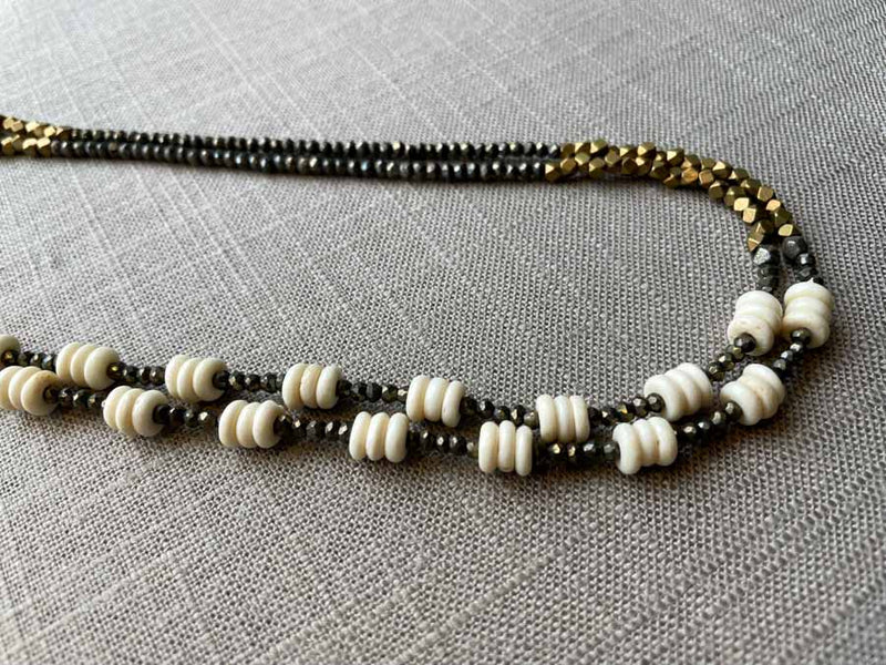 side view of gemstone bead necklace comprising beige bone, bronze and dark grey pyrite