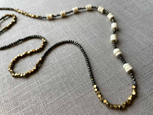 closeup of gemstone bead necklace comprising beige bone, bronze and dark grey pyrite