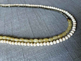 side view of gemstone bead necklace comprising blonde horn, white conch shell and dark grey pyrite