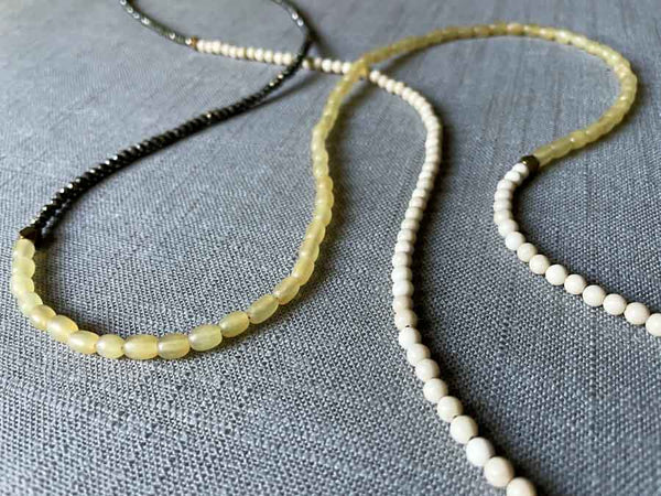 closeup of gemstone bead necklace comprising blonde horn, white conch shell and dark grey pyrite