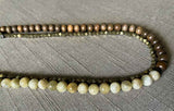 side view of gemstone bead necklace comprising exotic wood, off-white moonstone and dark grey rock pyrite