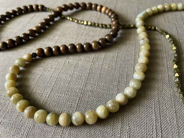 closeup of gemstone bead necklace comprising exotic wood, off-white moonstone and dark grey rock pyrite