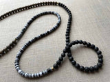 closeup of gemstone bead necklace comprising black lava stone, black and white vinyl discs and exotic wood