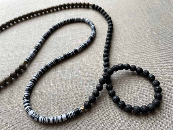 closeup of gemstone bead necklace comprising black lava stone, black and white vinyl discs and exotic wood