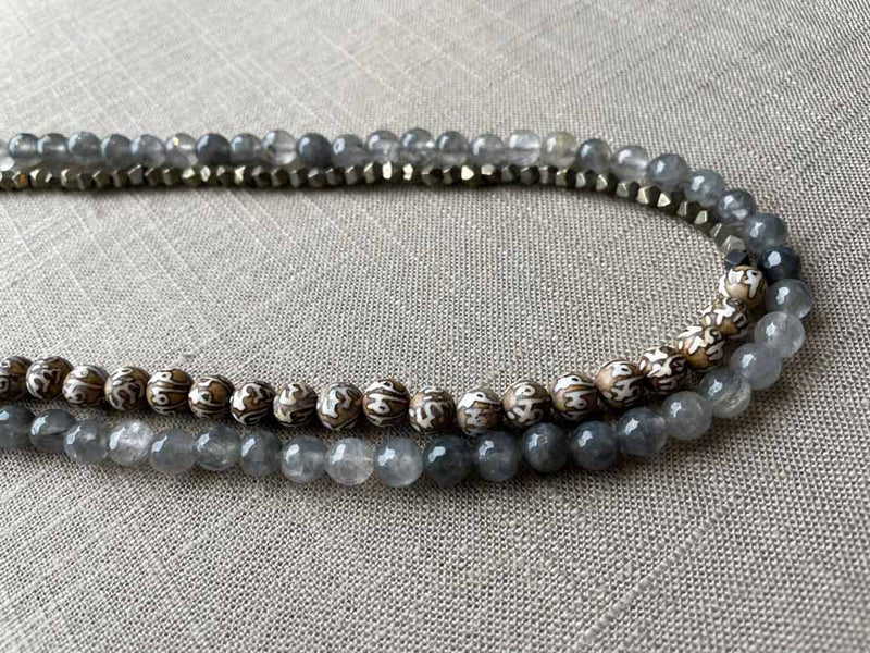 side view of gemstone bead necklace comprising tan prayer beads, black and white tourmalated quartz and dark grey pyrite