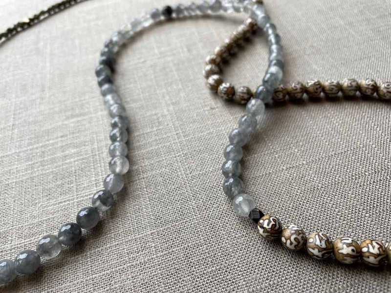 closeup of gemstone bead necklace comprising tan prayer beads, black and white tourmalated quartz and dark grey pyrite