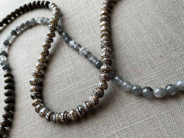 closeup of gemstone bead necklace comprising tan prayer beads, black and white tourmalated quartz and exotic wood