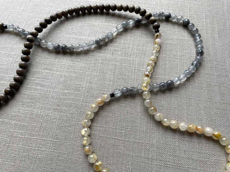 closeup of gemstone bead necklace comprising black and white tourmalated quartz, neutral rutilated quartz and exotic wood