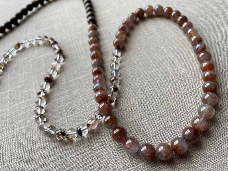 closeup of gemstone bead necklace comprising neutral shadow quartz, strawberry quartz and exotic wood