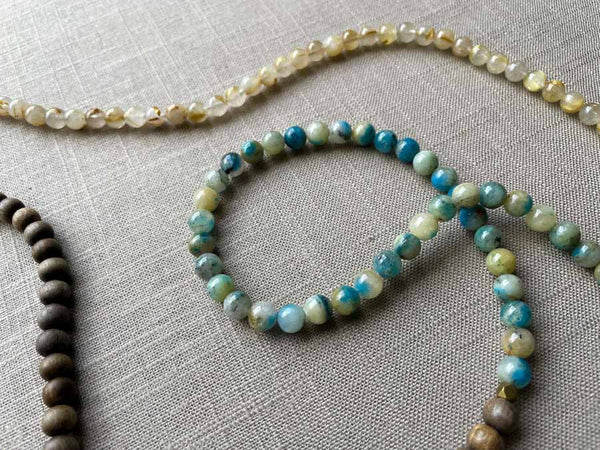 closeup of gemstone bead necklace comprising neutral rutilated quartz, blue azurite and exotic wood