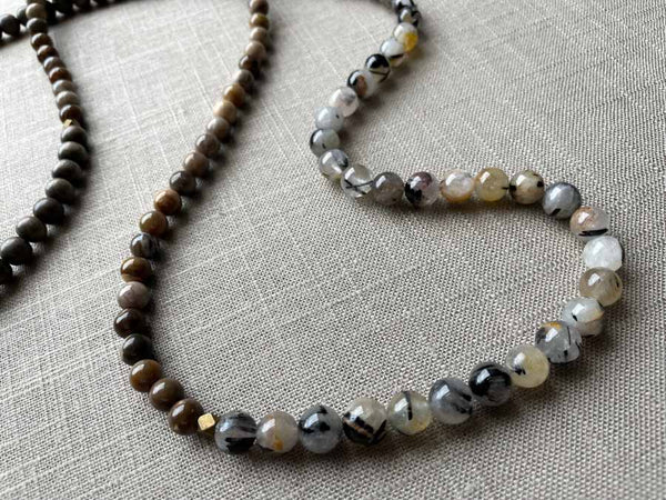 closeup of gemstone bead necklace comprising beige fossilized wood, black and white tourmalated quartz and exotic wood