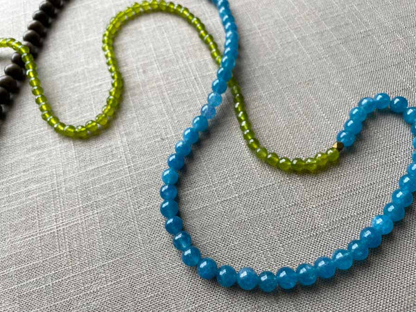 closeup of gemstone bead necklace comprising blue apatite, green peridot and exotic wood