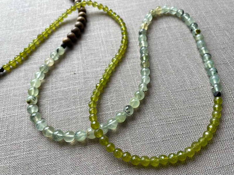 closeup of gemstone bead necklace comprising green prehnite, green peridot and exotic wood