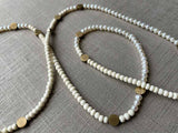 closeup of gemstone bead necklace comprising white pearl, white conch shell and bronze dot accents