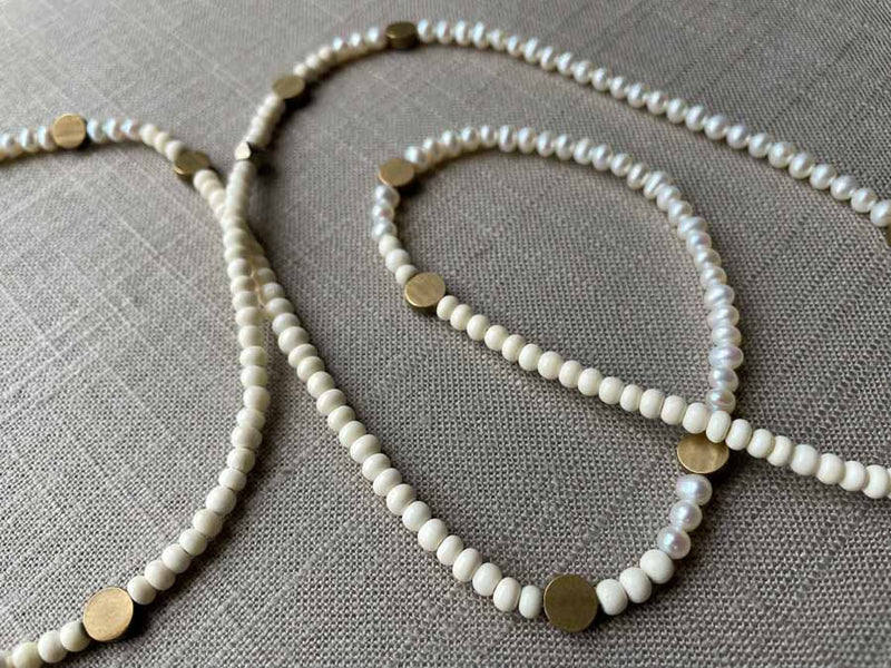 closeup of gemstone bead necklace comprising white pearl, white conch shell and bronze dot accents