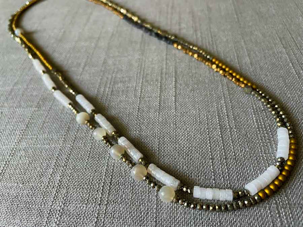 top view of gemstone bead necklace comprising white moonstone, white quartz, raw pyrite, dark bronze and gold hematite