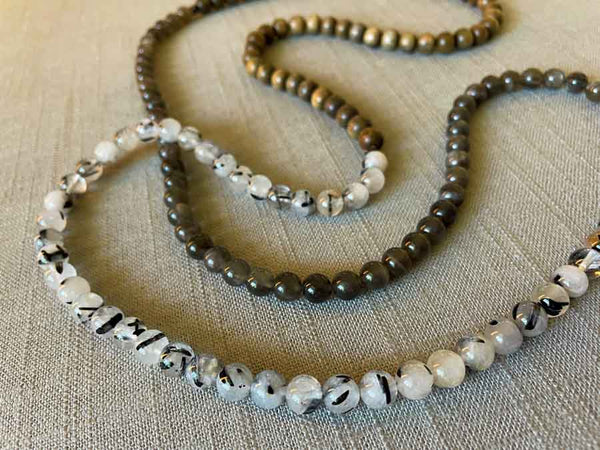 closeup of gemstone bead necklace comprising black and white tourmalated quartz, grey moonstone and exotic wood