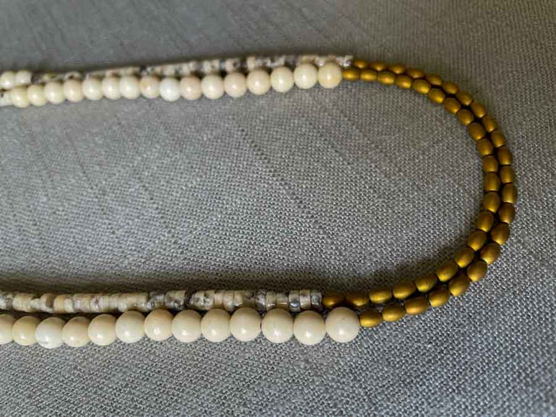 side view of gemstone bead necklace comprising black and cream feldspar, off-white fossil jasper and gold hematite