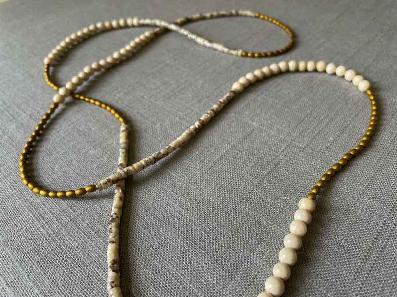 closeup of gemstone bead necklace comprising black and cream feldspar, off-white fossil jasper and gold hematite