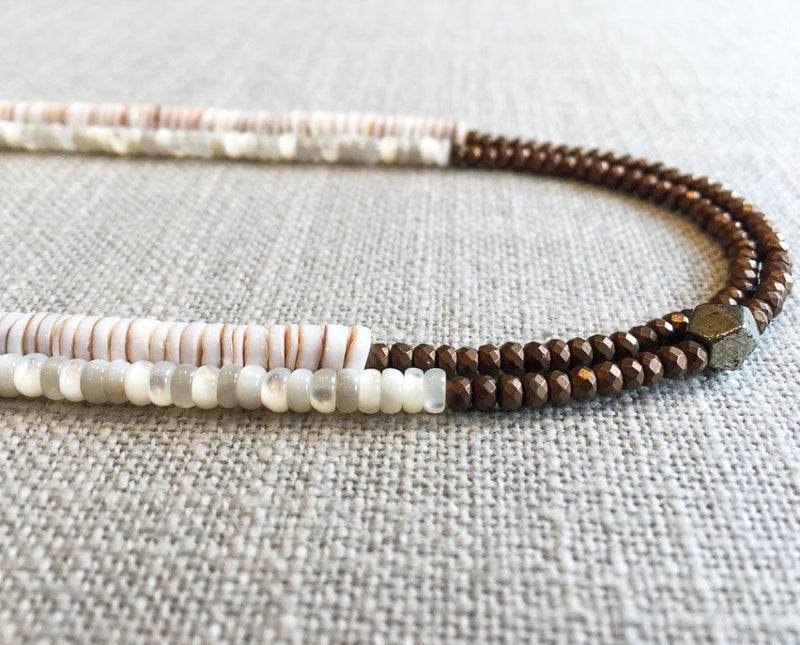 side view of gemstone bead necklace comprising white mother of pearl, bronze hematite and white shell