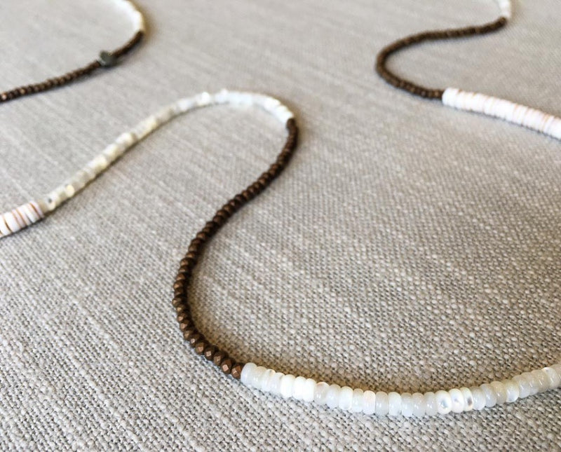 closeup of gemstone bead necklace comprising white mother of pearl, bronze hematite and white shell