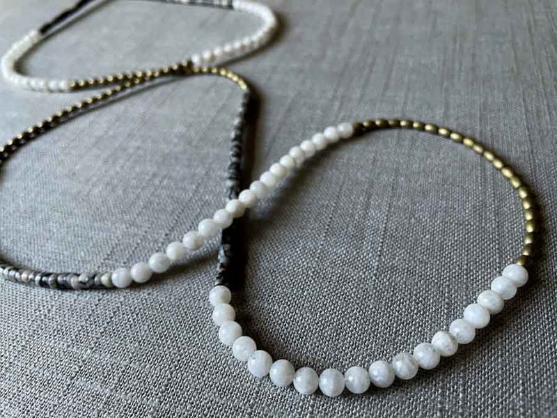 closeup of gemstone bead necklace comprising black and white feldspar, white moonstone and light gold hematite