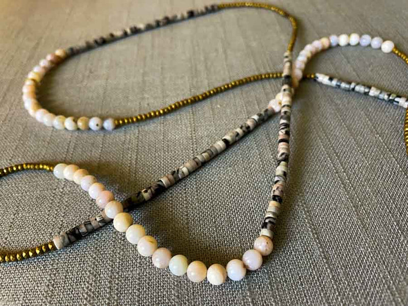 closeup of gemstone bead necklace comprising black/white/nude feldspar, pink opal and gold hematite