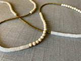 closeup of gemstone bead necklace comprising white moonstone , off-white fossil jasper and gold hematite