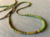 closeup of gemstone bead necklace comprising multicolored vinyl discs, green moss agate and light gold hematite