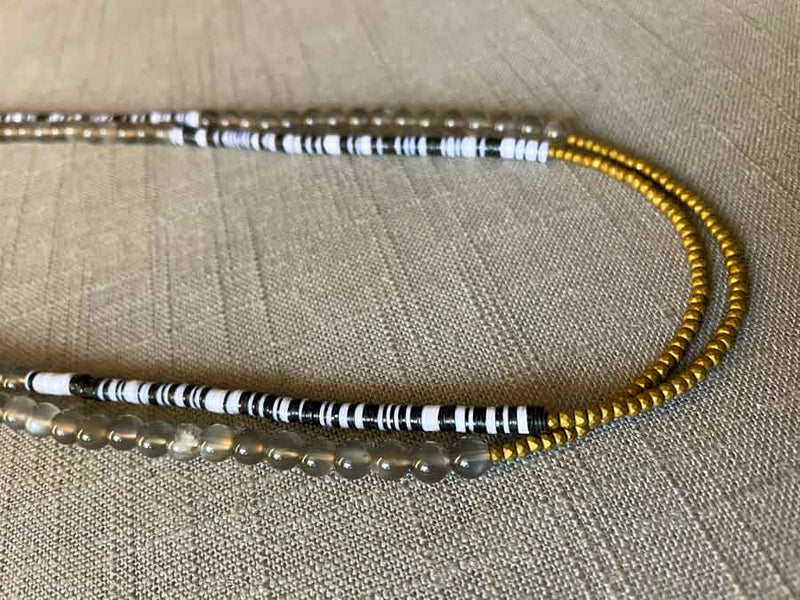 side view of gemstone bead necklace comprising black and white vinyl discs, grey moonstone and gold hematite