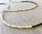 closeup of gemstone bead necklace comprising white mother of pearl, dark grey pyrite and rainbow moonstone