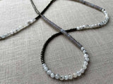 closeup of gemstone bead necklace comprising purple smoky quartz, black and white tourmalated quartz and dark grey pyrite