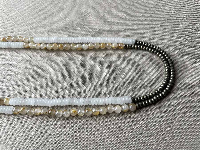 side view of gemstone bead necklace comprising white moonstone, neutral rutilated quartz and dark grey pyrite