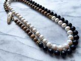 top view of gemstone bead necklace comprising white pearl, black onyx and exotic wood with antler clasp